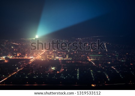 Night city. A bright lantern shines in the dark sky. Spotlight illuminates the darkness. Blue ray shines up.