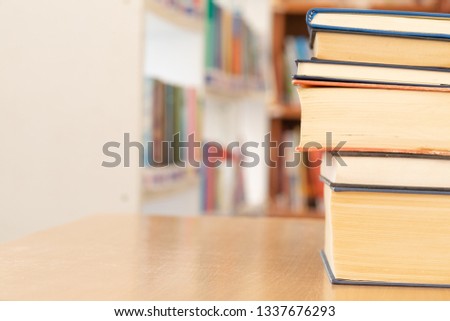 Book stack on wood desk and blurred bookshelf in the library room, education background, back to school concept 