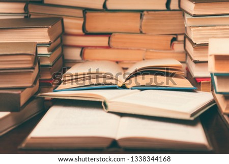 Education learning concept with open book and notebook on the table. Stack piles of books on reading desk and glasses in bookshelves background