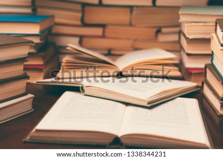 Old book in library with open textbook, stack piles of literature text archive on reading desk in school study class room background for education learning concept. Narrow depth of field