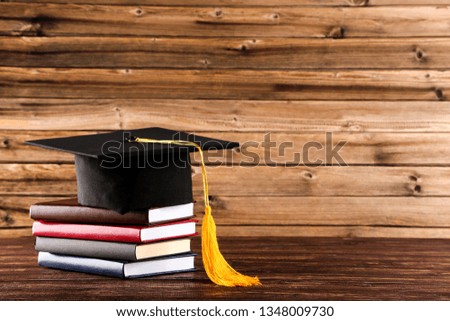 Graduation cap with stack of books on brown wooden table