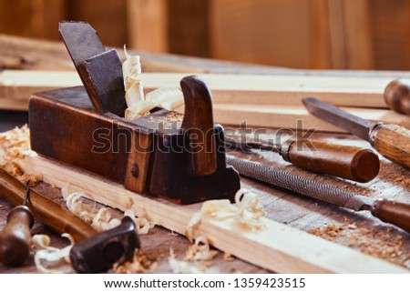 Wooden plane with rasp, file, hammer and chisels on a workbench with freshly planed planks of wood in a woodworking workshop