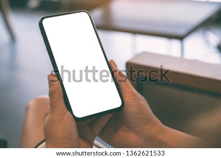 Mockup image of a woman holding black mobile phone with blank white screen in cafe