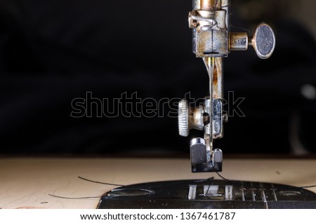 Close-up of a sewing machine with black thread and needle on a table with blurred background
