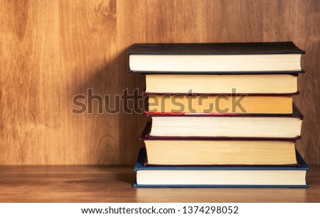 Pile of closed books on wooden shelf.