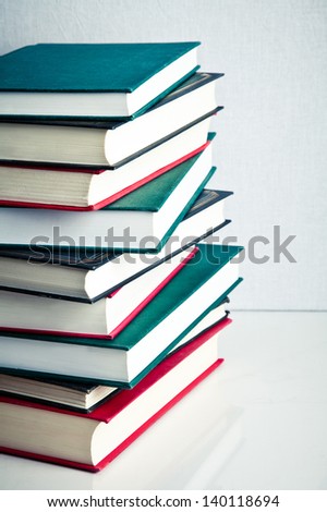 Stack of red, green and black books on white reflective surface