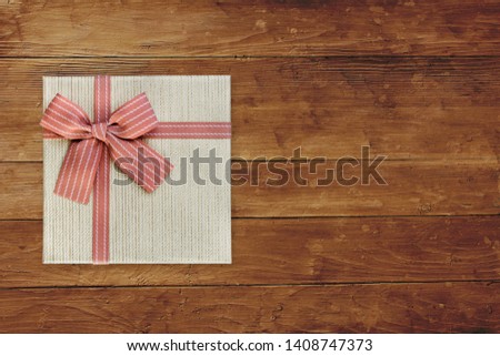 Gift box with pink ribbon over brown wooden background, top view with copy space