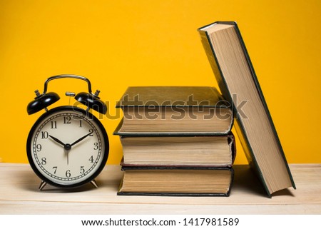 Retro alarm clock next to a stack of books on a yellow background. Reading books, school, library