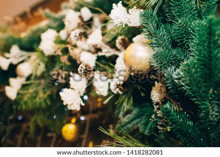 Golden ball Christmas ornament hanging on dry tree branch. Shining garland golden lights. Magical atmosphere. Macro photo of golden ball and light garland on Christmas tree