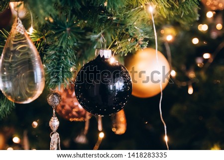 Golden ball Christmas ornament hanging on dry tree branch. Shining garland golden lights. Magical atmosphere. Macro photo of golden ball and light garland on Christmas tree