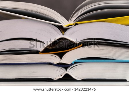 Four opened books on different colors are above each other on the white table, grey background. International Students Day. Back to school