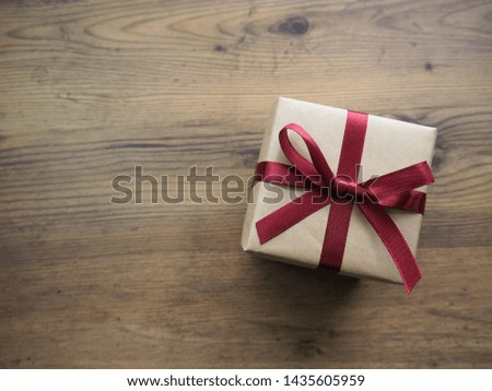 Beige color simple gift box with red ribbon on brown wooden background