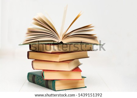 stack of books lies on a white wooden table, one book is opened, with text.