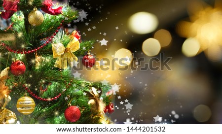 Festive green Christmas tree decorated with gold and red toys balls and bows with soft focus in evening and beautiful dark blurred defocused sparkling background with golden highlights, copy space.