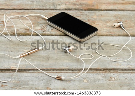 Smartphone with earphones on wooden boards. Mobile phone with blank screen and earbuds on vintage wooden background. Modern audio technology.