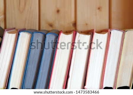 Row of different old books in hard color covers standing on bookshelf against brown wooden wall front view close up 