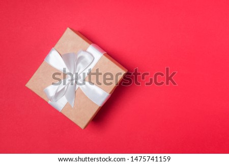Giftbox with white ribbon on the red background, top view.