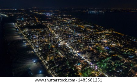 night aerial view city. Evening lights resort city. Adriatic Sea near town of Lignano Sabbiadoro Italy. Sea top coastline Europe. Black grained background and dark silhouettes of houses.