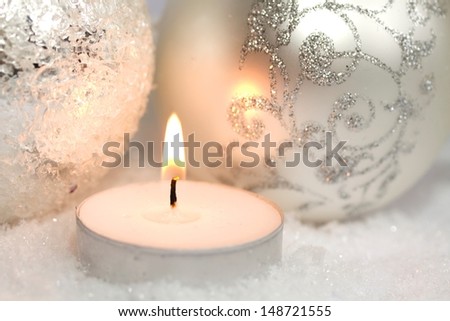 silver Christmas ornaments and a burning candle in the snow