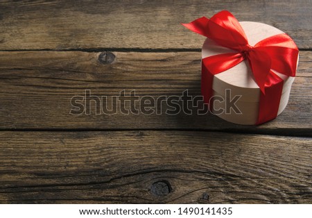 Box with red ribbon bow gift on wooden background