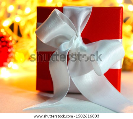 Christmas gift, red box with white ribbon on defocused lights background.