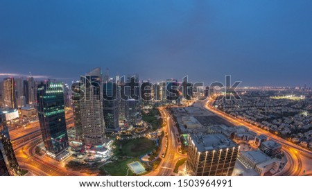 Jumeirah Lake Towers residential district aerial day to night transition timelapse near Dubai Marina. Illuminated modern skyscrapers and park from above