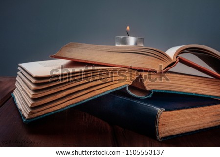 A stack of old books with a burning candle and a place for text, selective focus