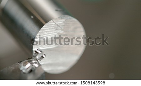 MACRO, DOF: Detailed shot of a lathe tool shaving the edge of a shiny metal rod. Twisted shavings of aluminium spiral off a shiny workpiece processed by a CNC machine. Rotating cylinder and blade.