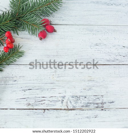 Branches of spruce and red berries on a white square wooden background. Christmas composition. Selective focus. Concept for your mockup and project. Flat lay, copy space, top view.
