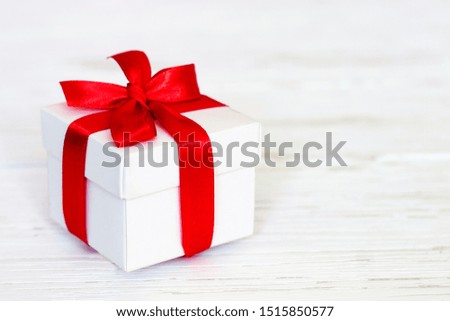 White gift box with a red ribbon on a white wooden background, copy space. Greeting card concept. Gift concept
