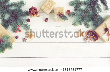 Christmas background with fir twigs, gifts, red berries, cones, sinnamon sticks and Xmas decor on white wooden background top view. vintage toned. Copy space
