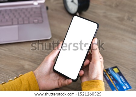 Women hands holding Mobile Phone with blank screen and Credit Card on office desk and using mobile phone for Online Shopping, Internet Banking, Online Trading, E Commerce Concept. with clipping path