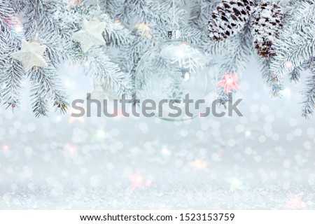 christmas tree branch decorated with glass ball and silver stars. white snowy winter background