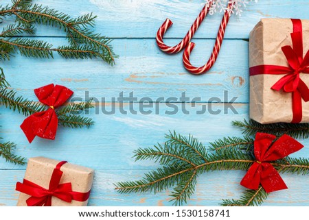 gift box present wrapped, holiday candies, craft paper with red bow  with fur spruce pine coniferous branches, on the blue painted wooden background close up