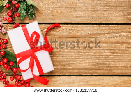 Gift box and holly ilex berries top view background. New year, Xmas present. Festive wooden backdrop with copyspace. Christmas composition with decorative elements. Winter holidays concept