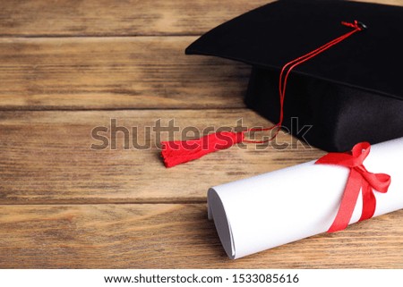 Graduation hat and student's diploma on wooden table, space for text