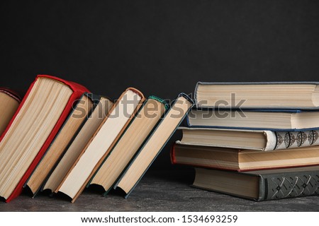 Stack of hardcover books on grey stone table against black background