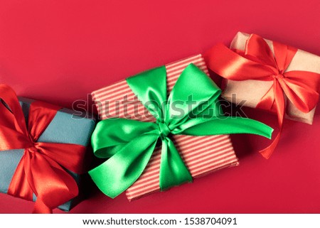 Three bright christmas gifts with traditional color atlas ribbons and bows on solid red background, festive concept