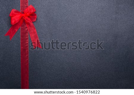Red ribbon and bow on the black surface. Empty space for text