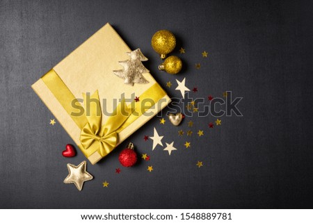 Top view of golden gift boxes with shiny satin bows and glittering christmas tree toys as attributes of party on black chalk board background with copy space