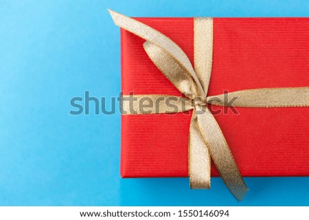 holiday, greeting and surprise concept - christmas red gift box with golden bow on blue background