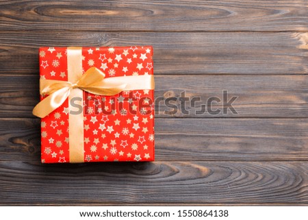 Beautiful gift box with a colored bow on the dark wooden table. Top view with copy space for you design. Christmas concept.