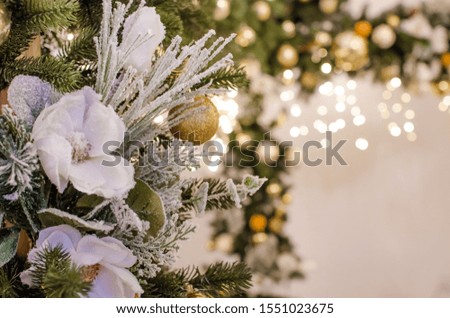 
A beautiful Christmas bouquet of fir branches with colorful balls and flowers, a garland stands in the living room. Photo in warm tint.