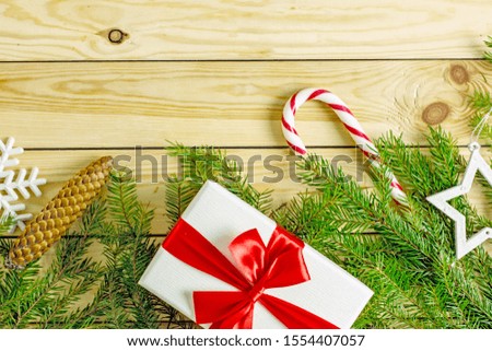 Christmas gift box with a red bow on a wooden background surrounded by fir branches. Close-up, top view. Background about christmas and new year. Frame with fir branches on a wooden background 