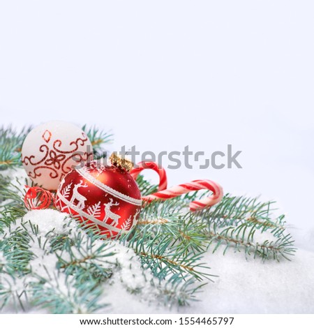 Red and white Christmas bauble and candy canes on abstract winter blue white background with natural fir twigs under snow with text space above. Merry Xmas and a Happy New Year!