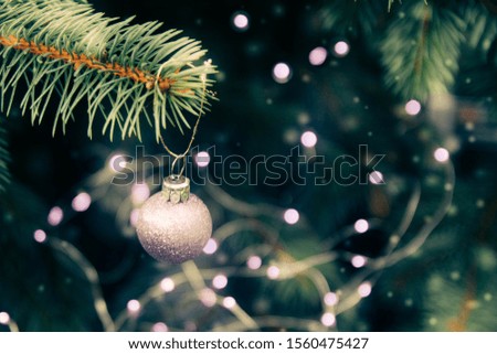 The tree is decorated for Christmas with a purple garland with bulbs, a ball. Copy space. Glare, light, on Christmas tree. Beautiful background of natural spruce. It's snowing, snowflakes are flying.