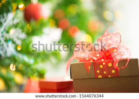 Brown gift box and a red bows with blurred Christmas tree on the background