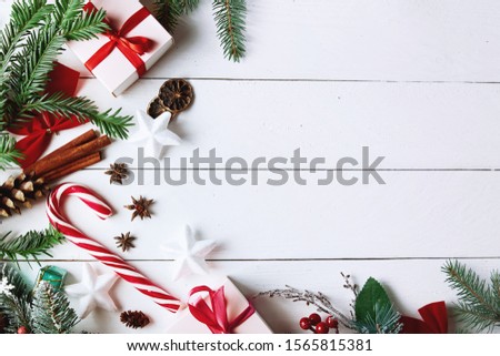 Beautiful Christmas composition on white background with Christmas gift boxes, snowy fir branches, conifer cones, holiday decoration, caramel stick and red berry. Top view, copy space.