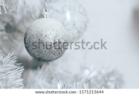 Silver bauble hanging on white Christmas tree. Home interior, white wall background. Ball, closeup, New Year, celebration, holiday, copy space