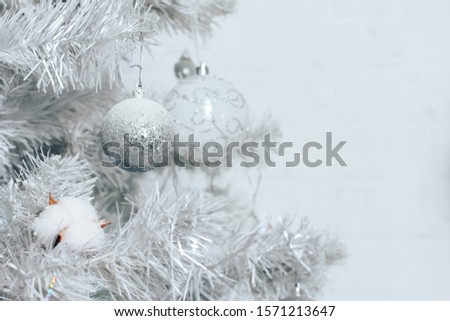 Silver bauble hanging on white Christmas tree. Home interior, white wall background. Ball, closeup, New Year, celebration, holiday, copy space